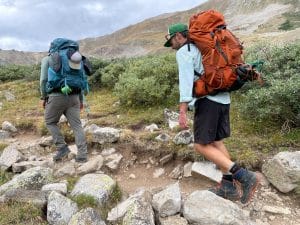 Two hikers wearing the Osprey Atmos pack in blue and Osprey Aether pack in orange.