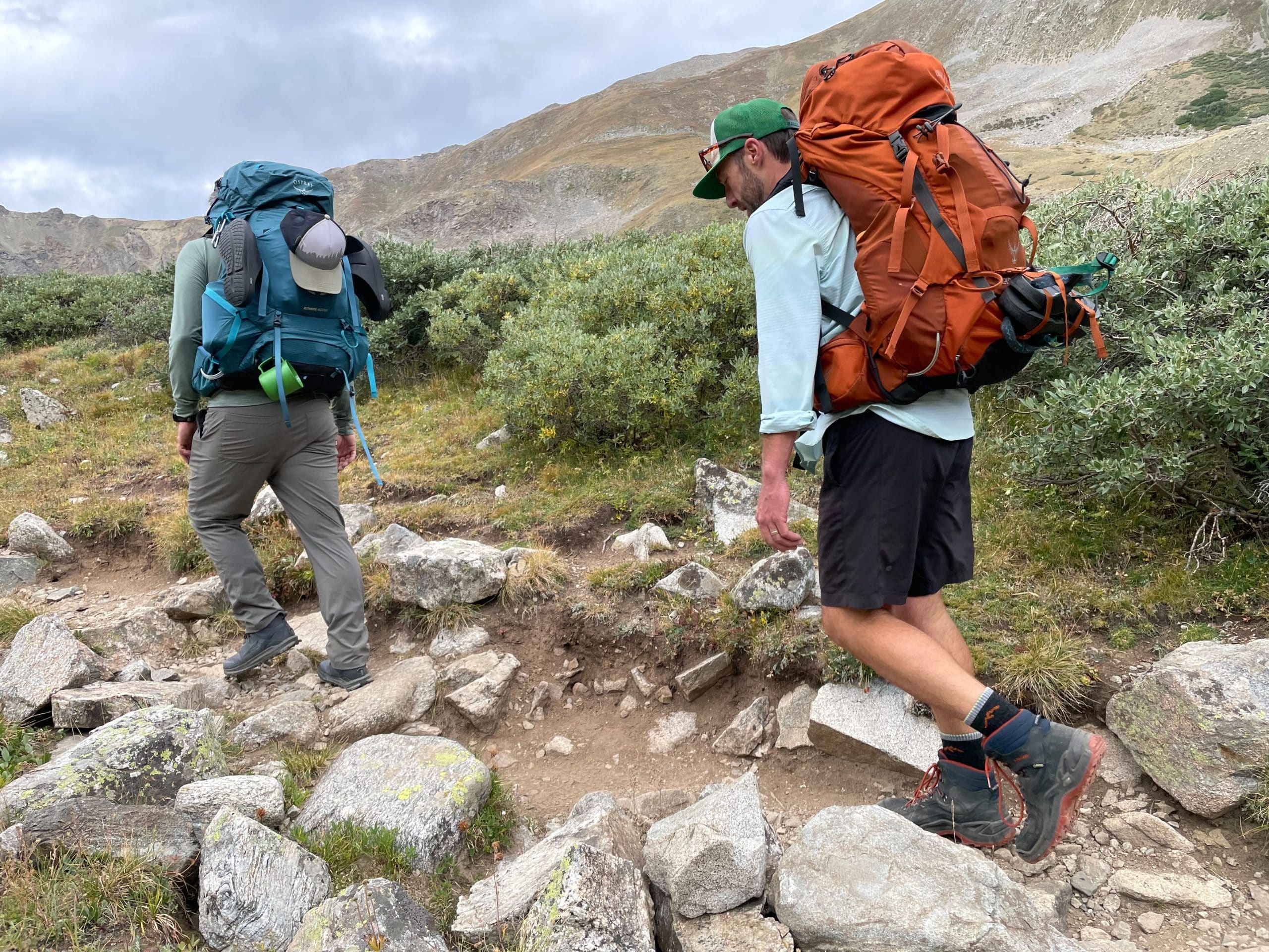 Two hikers wearing the Osprey Atmos pack in blue and Osprey Aether pack in orange.