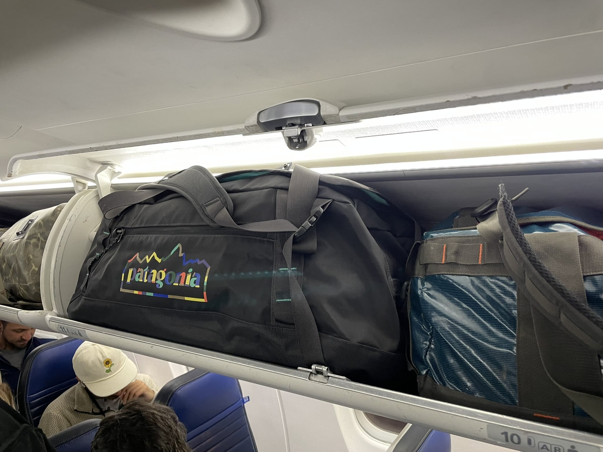 A Patagonia Black Hole Duffel 55L in an airplane overhead bin.