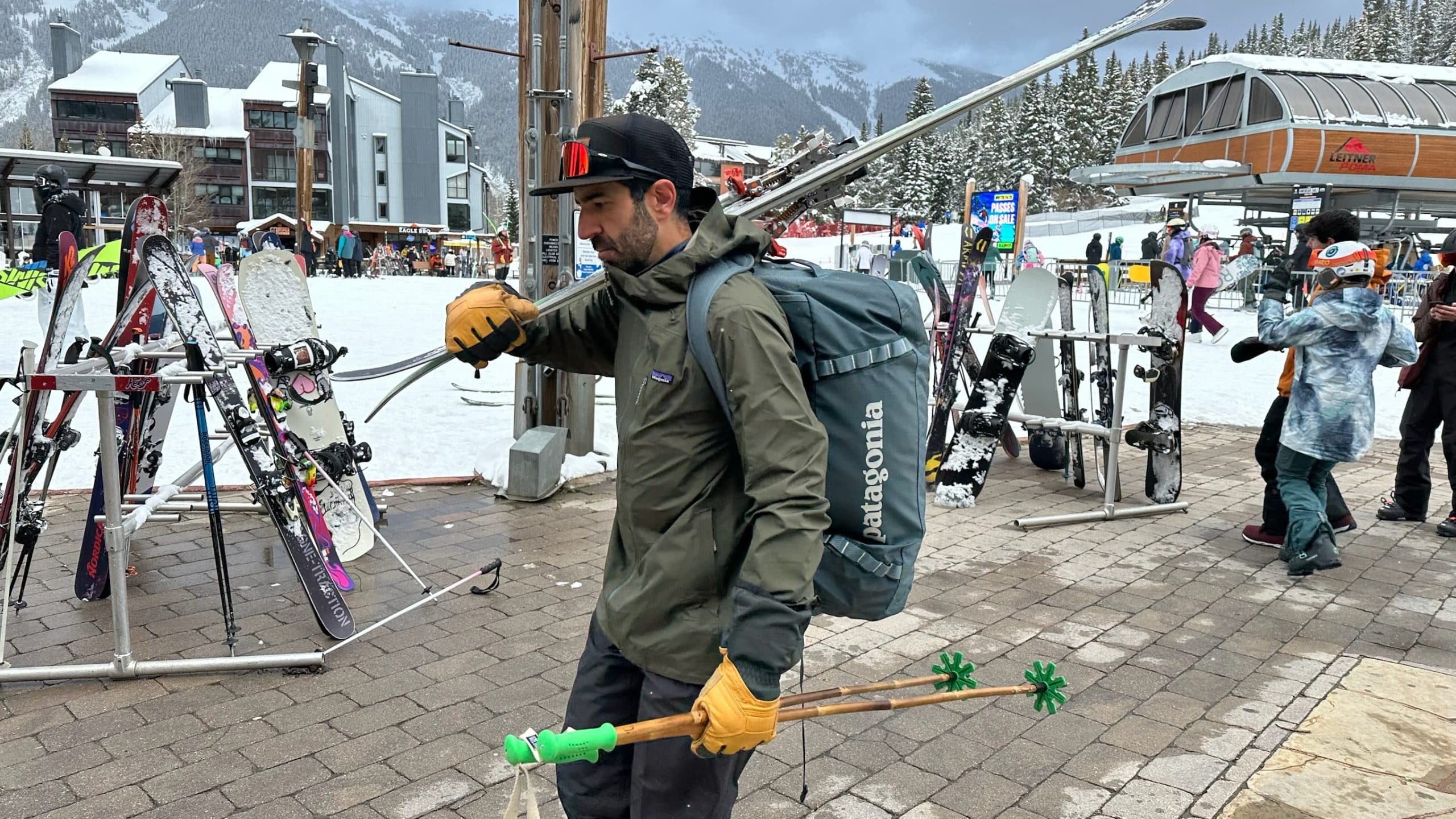 Image of a man carrying skis and a Patagonia Black Hole Duffel 70L as a backpack.