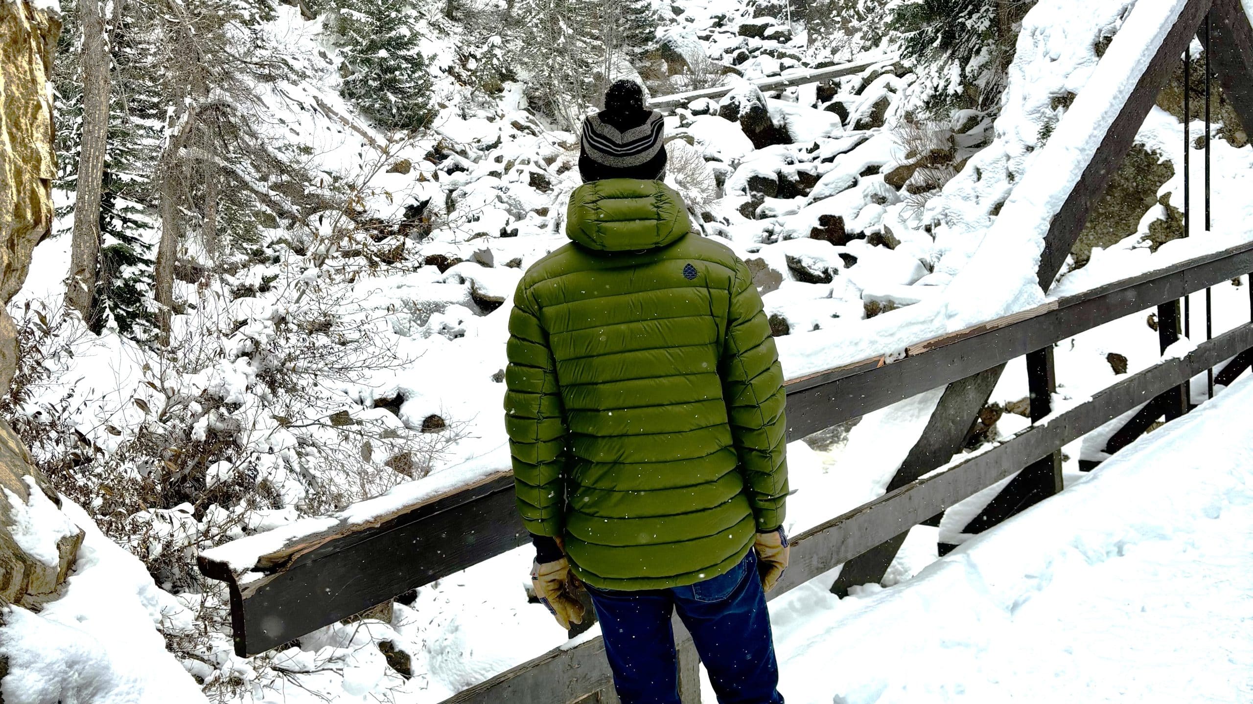 Image taken behind someone standing on a snowy bridge wearing the Stio Hometown Down hooded jacket.