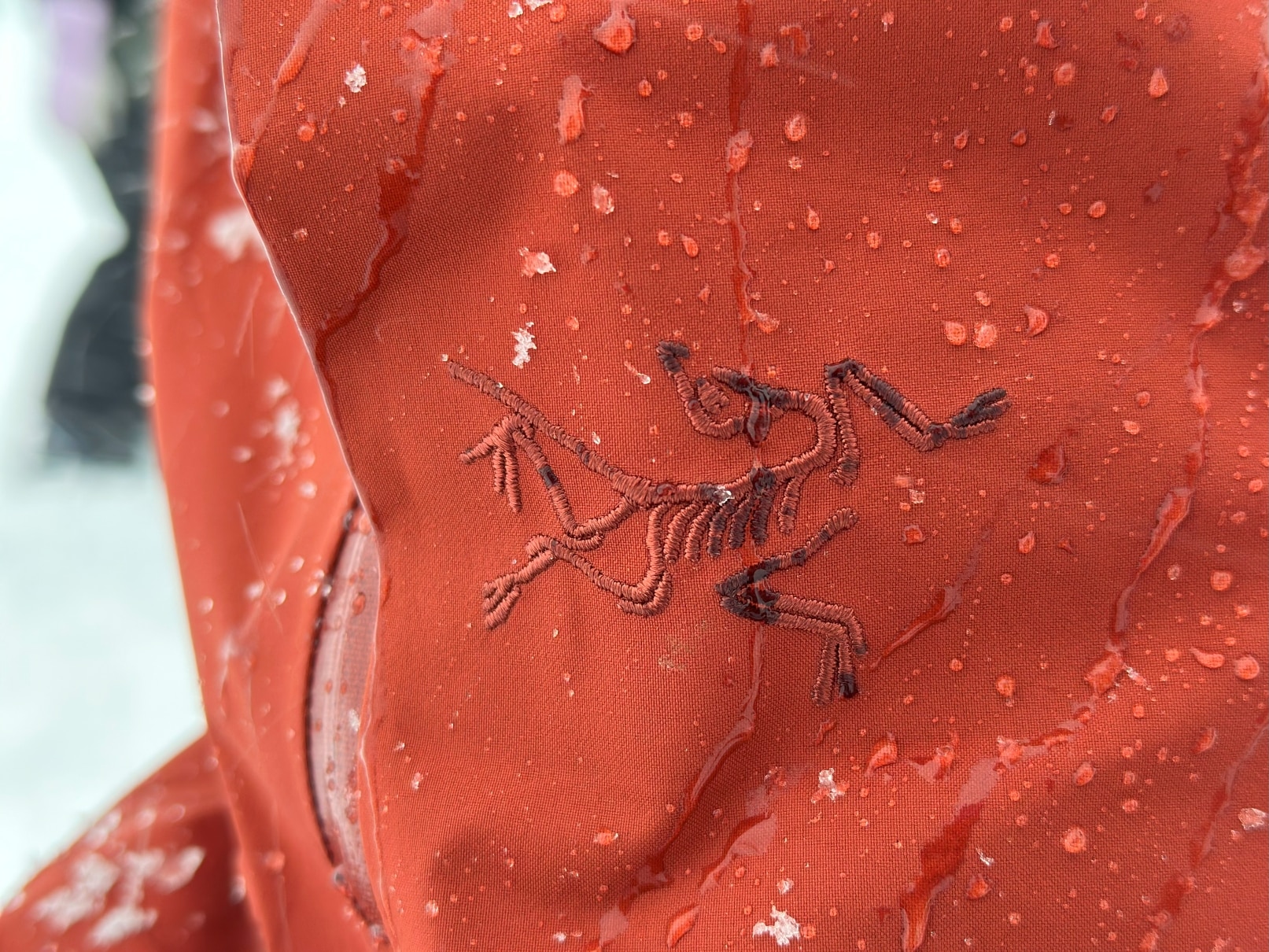 Closeup image showing the Arc'teryx logo on a jacket covered in water drops.