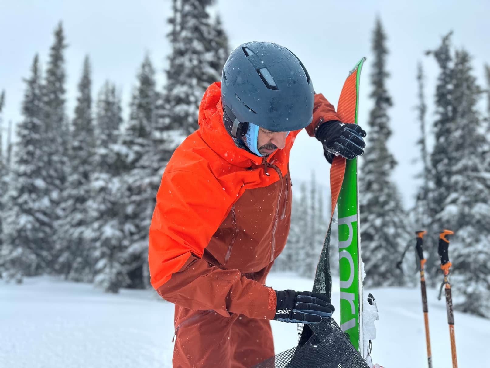 A backcountry skier puts skins on his skis while wearing the Arc'teryx Rush ski jacket and pants.