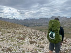 A backpacker looking at mountains in the distance while wearing the Osprey Aether 55 backpack.