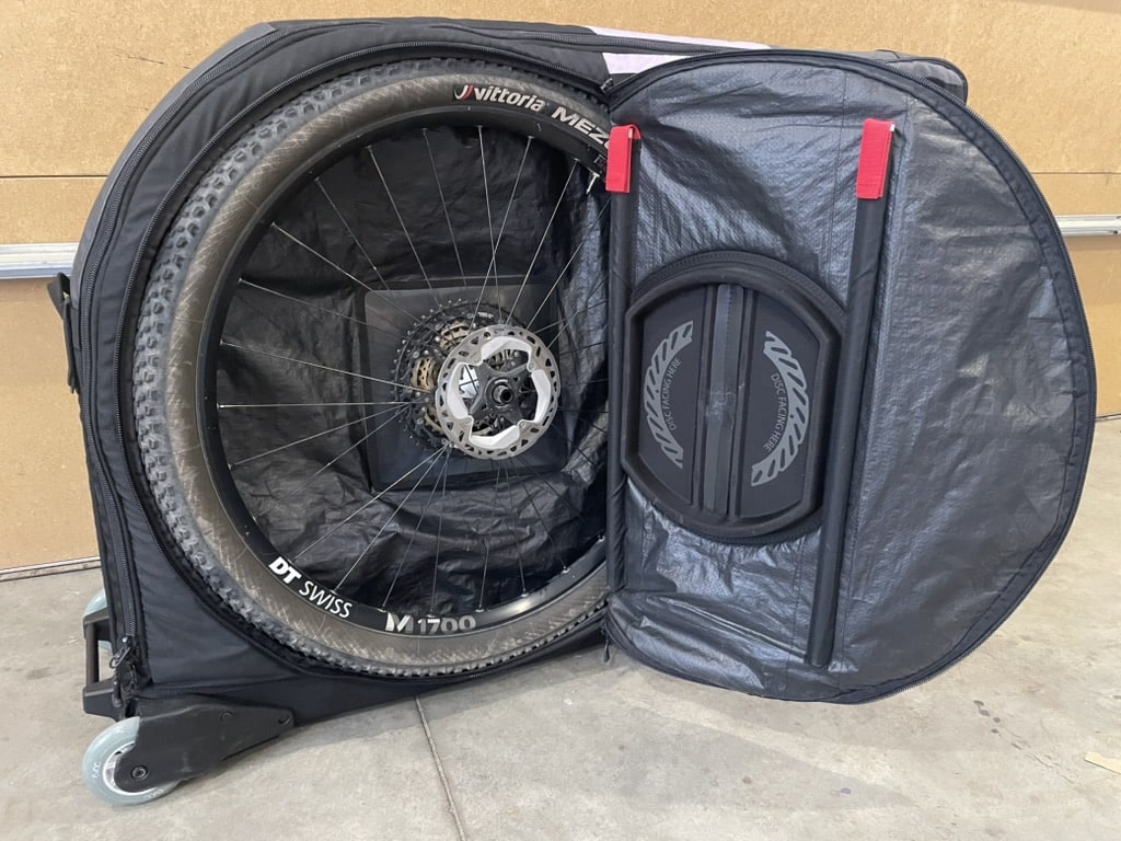 A mountain bike wheel inside the exterior wheel compartment of the Evoc Travel Bag Pro.