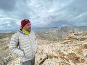 A man standing on a mountain peak wearing the Arc'teryx Cerium.