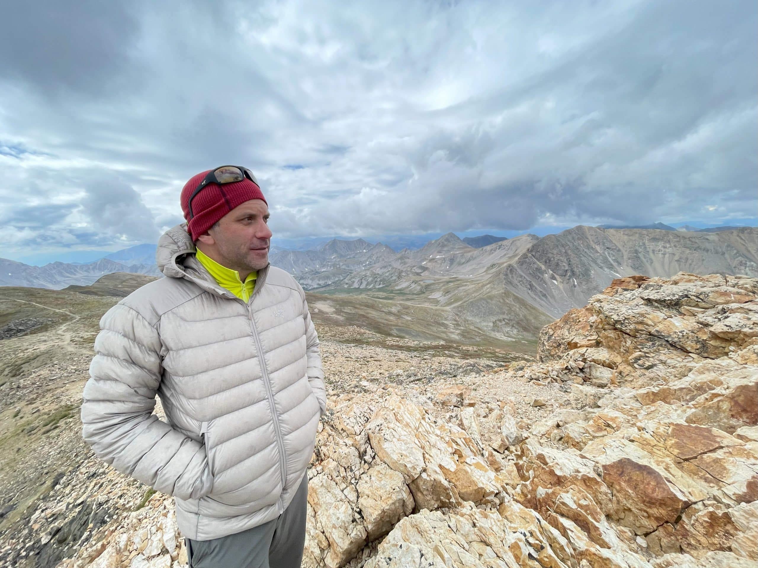 A man standing on a mountain peak wearing the Arc'teryx Cerium.