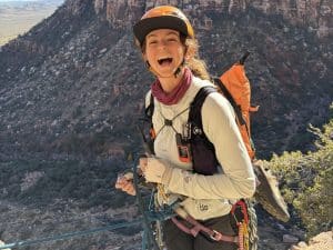 A woman rock climbing with the Arc'teryx Konseal Shoe attached to her backpack.