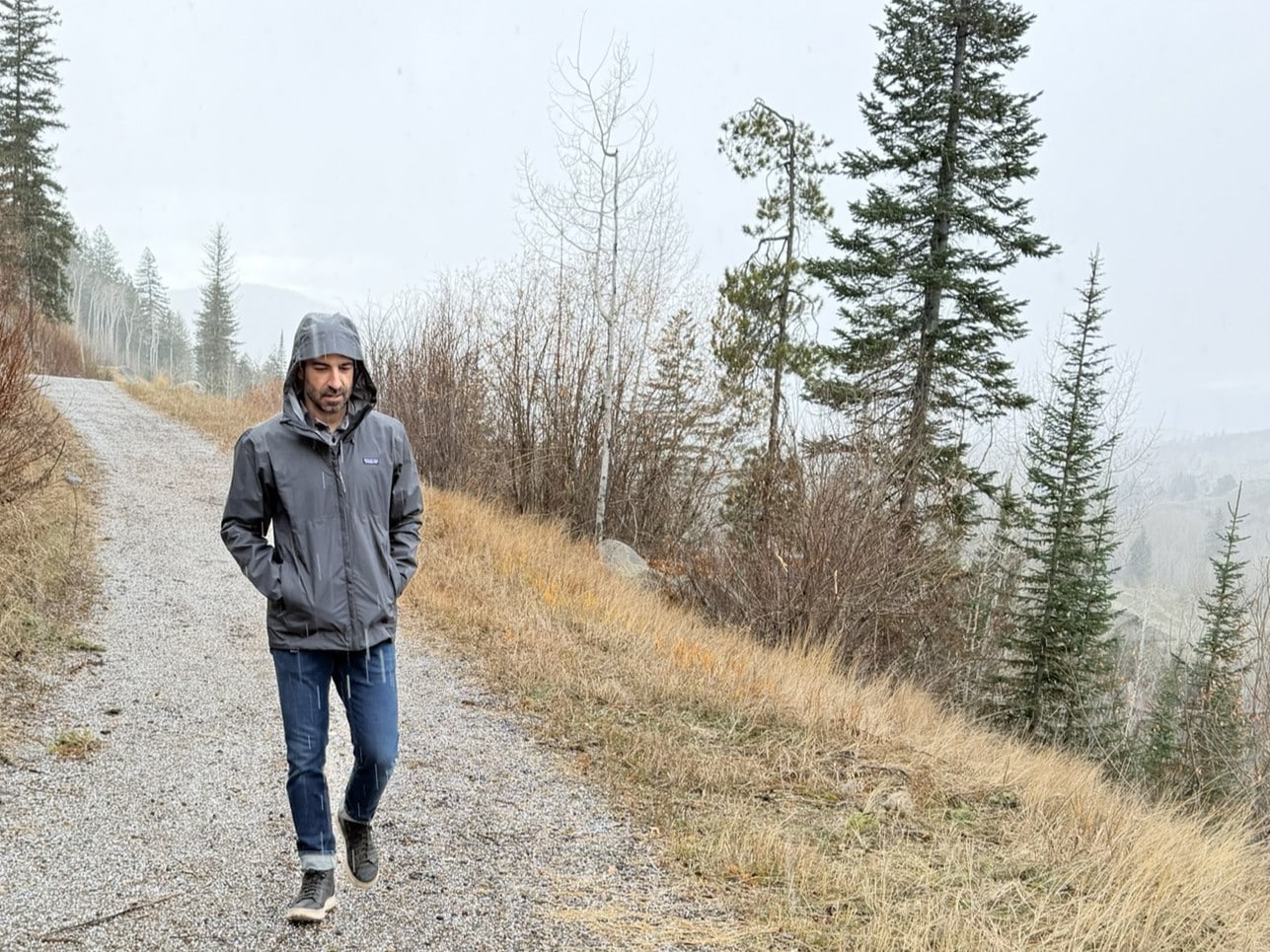 A man walking in cold rain wearing the Patagonia Torrenshell 3L rain jacket.